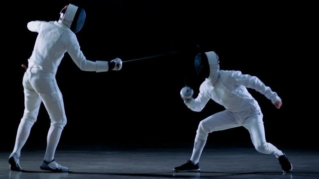 Two Professional Fencers Show Masterful Swordsmanship in their Foil Fight. They Dodge, Leap and Thrust and Lunge. Shot Isolated on Black Background  and in Slow Motion.