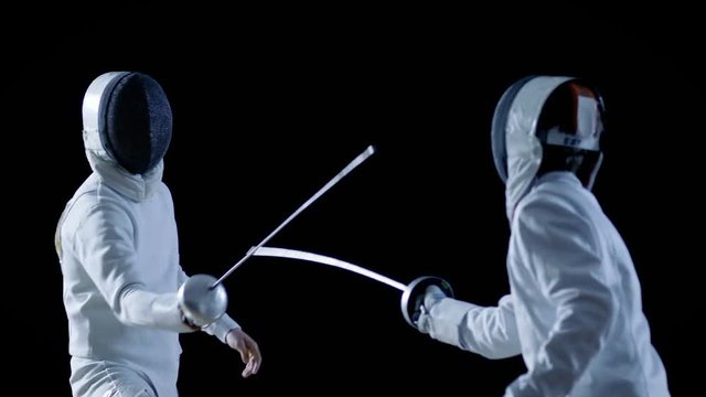 Two Professional Fencers Show Masterful Swordsmanship in their Foil Fight. They Attack, Defend, Leap and Thrust and Lunge. Shot Isolated on Black Background  and in Slow Motion. 