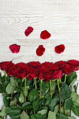 Red roses and petals on a light wooden background, top view