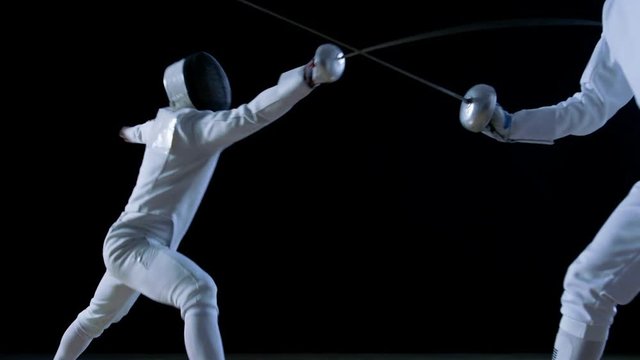 Two Professional Fully Equipped Fencers Expertly Fight with Foils. They Attack, Defend, Leap, Thrust and Lunge. Shot in Slow Motion and on Isolated Black Background. 