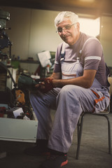 Senior man in workshop. Man sitting next to the tools and looking at camera.