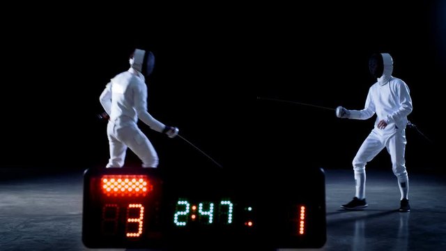 On the Championship Two Professional Fully Equipped Fencers Expertly Fight with Foils while Scoreboard Keeps the Scores of Hits. They Attack, Defend, Leap, Thrust and Lunge. 