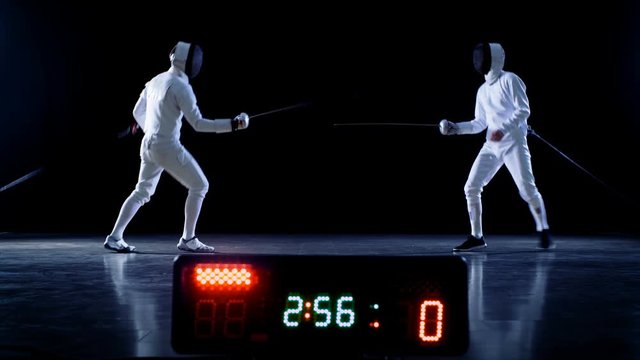 On the Championship Two Professional Fully Equipped Fencers Expertly Fight with Foils while Scoreboard Shows Hits. They Attack, Defend, Leap, Thrust and Lunge. Shot Isolated on Black Background. 