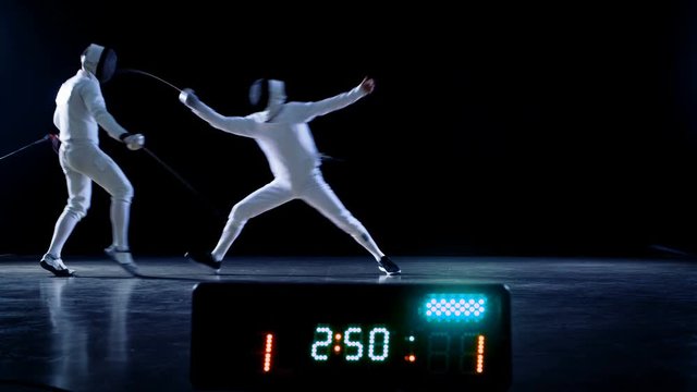 On the Championship Two Professional Fully Equipped Fencers Expertly Fight with Foils while Scoreboard Shows Hits. They Attack, Defend, Leap, Thrust and Lunge. Shot Isolated on Black Background. 