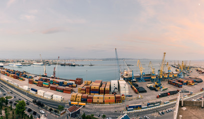 Panorama of the cargo terminal of the international port of Durres at sunset. Unloading of the tanker by cargo cranes. A platform for storing sea freight containers.