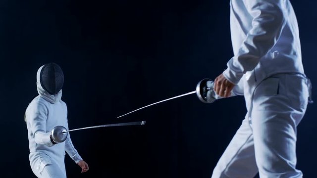 Two Professional Fully Equipped Fencers Expertly Fight with Foils. They Attack, Defend, Leap, Thrust and Lunge. Shot Isolated on Black Background. 