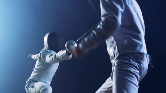 Two Professional Fully Equipped Fencers Expertly Fight with Foils. They Attack, Defend, Leap, Thrust and Lunge. Shot Isolated on Black Background. 