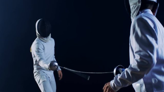 Two Professional Fully Equipped Fencers Expertly Fight with Foils. They Attack, Defend, Leap, Thrust and Lunge. Shot Isolated on Black Background. 