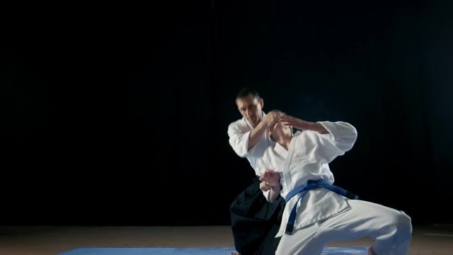 Martial Arts Master Wearing Traditional Samurai Hakamas Teaches Young Student Aikido Technique Defening Himself From Attack from the Back. Shot Isolated on Black Background and in Slow Motion. 