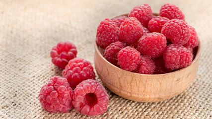 Ripe raspberry in wooden bowl on burlap background