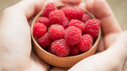 Female hands hold fresh organic raspberry in small wooden bowl