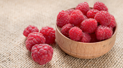 Ripe raspberry in wooden bowl on burlap background