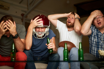 Four friends watching american football game on television, feeling frustrated