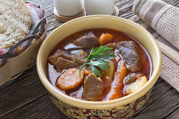 Stew with meat and vegetable in ceramic bowl on table