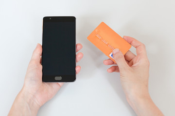 Female hands holding a phone with an isolated screen and a credit card over the desk in the office