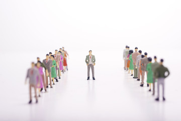 Miniature people in two lines across to each other with boss in the middle over white background.