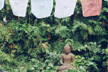 Buddha sculpture on green nature and buddhist prayer flags