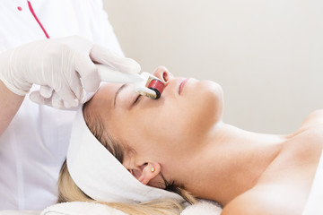 The woman undergoes the procedure of medical micro needle therapy with a modern medical instrument derma roller. 