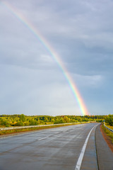 Asphalt road among the fields against a blue sky with a rainbow