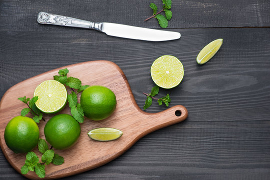 Fresh limes on cutting board on wooden table. Top view, background.