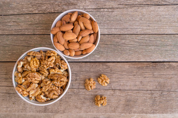 Two ceramic bowls full of walnuts and almonds on the wooden background