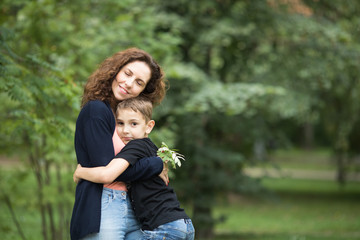 A mother with her son are in the green park giving warm hugs to each other.