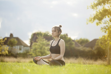 Fototapeta premium Young woman doing yoga and meditating in park