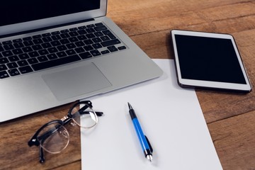 Digital tablet, laptop, paper, pen and spectacles on wooden
