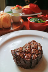 Grilled Tenderloin Steak on White Plate with Blurred Side Dishes in Background  