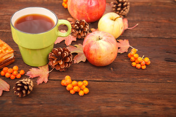 autumn composition. still life. berries of mountain ash, pine cones, fallen leaves and a cup of tea on a background of wood.