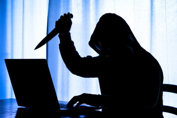 Cyber stalker online holding knife at laptop  - Concept of internet harassment with silhouette of dangerous hooded man                       