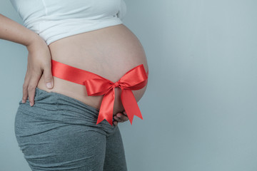 Closeup pregnant belly with red ribbon, Happy pregnant woman Concept.