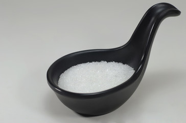White sugar in a black spoon. Selective focus
