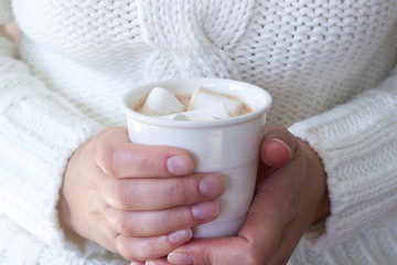 Fototapeta na wymiar Hot homemade cocoa with marshmallow in the hands of a woman. Woman in a white sweater. Rustic style, selective focus.