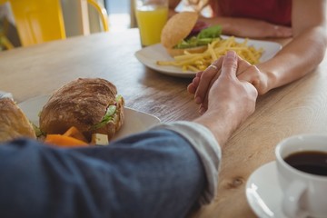 Cropped image of couple holding hands in cafe
