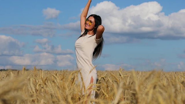 Young Happy brunette in yellow glasses is dancing in a wheat field