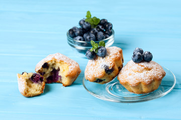 Homemade baked muffin with blueberries, fresh berries, mint, powdered sugar on blue wooden background. Top view.