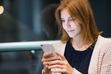 beautiful young red-haired woman using smartphone or cell phone at night on street