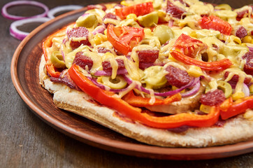 Pizza with salami, tomatoes, bell pepper, onion, green olives, corn, cheese and spices on brown wooden background. Close up view