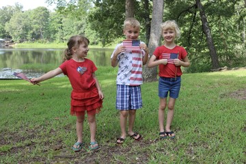 Three happy children waving American flag in patriotic clothes whilst celebrating the Fourth of July