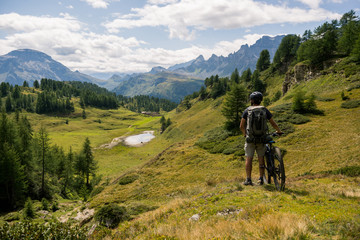 Young adult active man on mountain wearing bike helmet and backpack looking at scenic panorama...