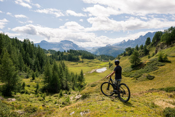 Young adult active man on mountain wearing bike helmet looking at scenic panorama holding electric...
