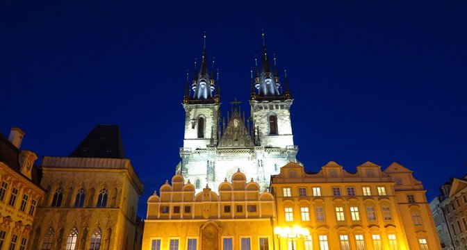 Prague Tyn Church towers over Baroque buildings in Old Town Square at night
