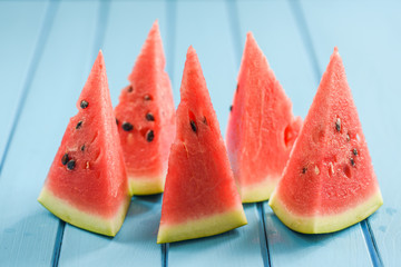 Fresh juicy watermelon with seeds cut into triangles on bright blue background