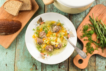 Big plate of tasty vegetable soup with meatballs served with rye bread and fresh herbs. Russian cuisine.