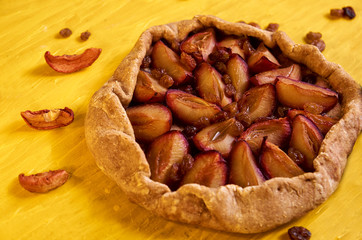 Sugar free pie with plums and raisins on yellow wooden background close up decorated with brown raisins and dried pieces of apple. Side view