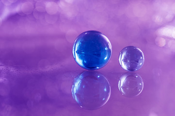Two blue glass balls on a glass table. Glass balls on a purple background with reflection.
