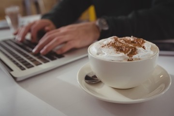 Cropped hands of businessman using laptop by coffee cup