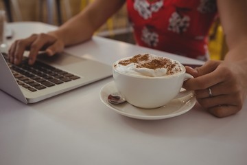 Midsection of woman with coffee using laptop