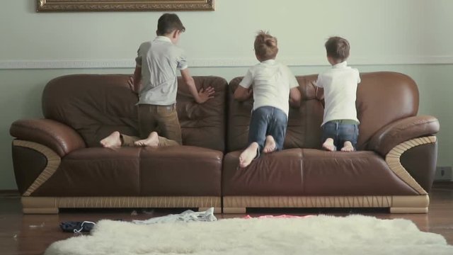 Three cute brothers jumps on a sofa in slowmotion